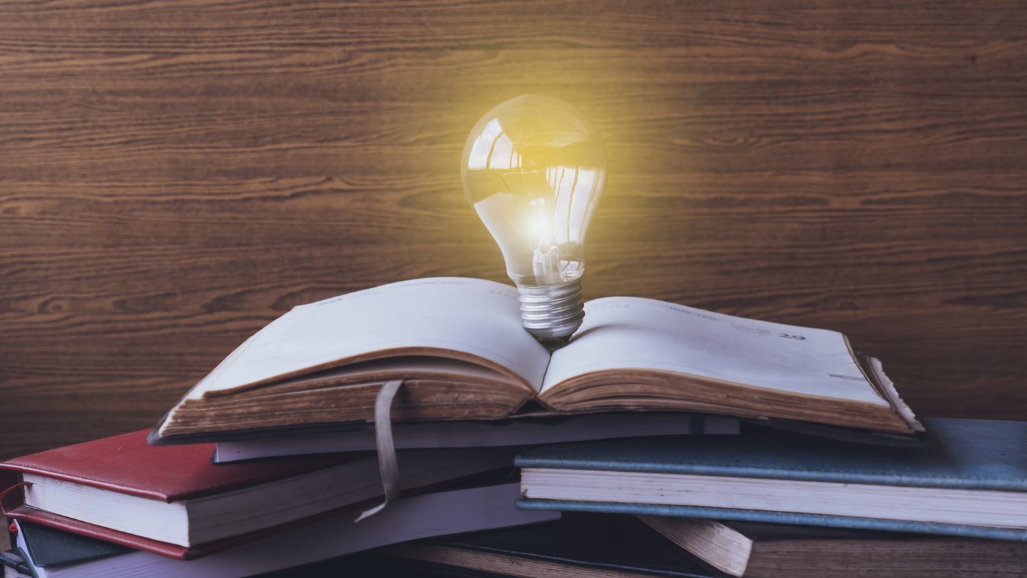 Ampoule allumée posée sur un livre ouvert, au sommet d’une pile de livres