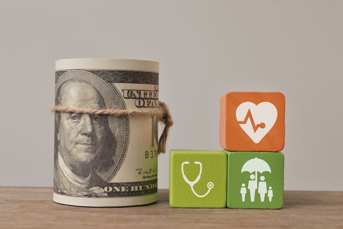 Rouleau de billets à côté de trois cubes illustrant la santé, les soins et la protection de la famille