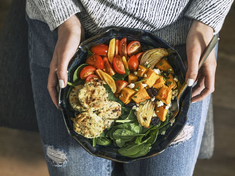 Bol de légumes rôtis, tomates et pousses d’épinards tenu à deux mains